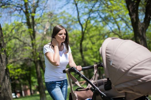 Young mother walking and pushing a stroller in the park.
