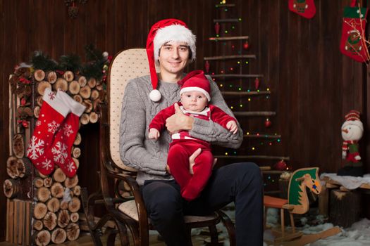 A man with a child dressed as Santa Claus on an armchair by a wooden fireplace on New Year's Eve.