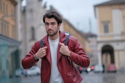 beautiful guy with red leather jacket and backpack in the center of reggio emilia