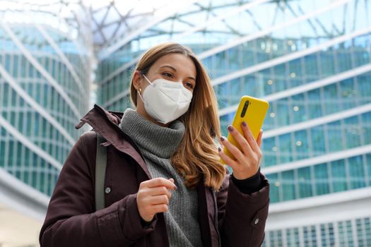 Business woman covering face with protective mask holding mobile phone with modern city background. Technolgy, growth, health care concept.
