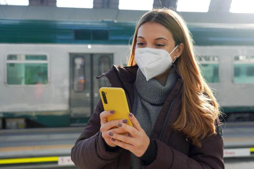 Young woman with medical face mask buying ticket online with smartphone on train station