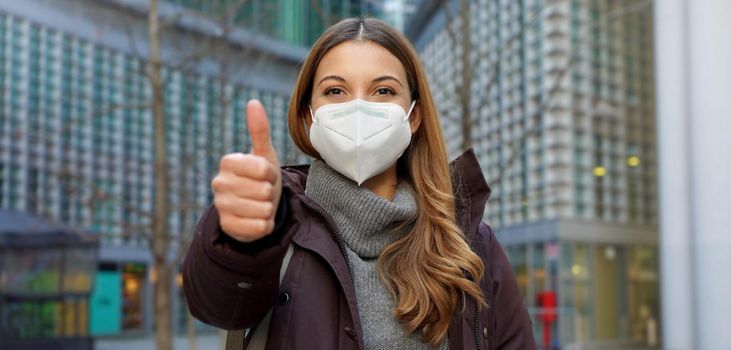 Panoramic banner cropped view of thumbs up woman wearing protective face mask and winter clothes in the city