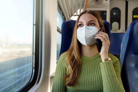 Young business woman wearing protective mask required for public transport talking with phone sitting in the train