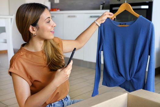 Checking product before delivering to customer. Stylish small business owner woman using smartphone app to sell clothing online. Small business entrepreneur. 