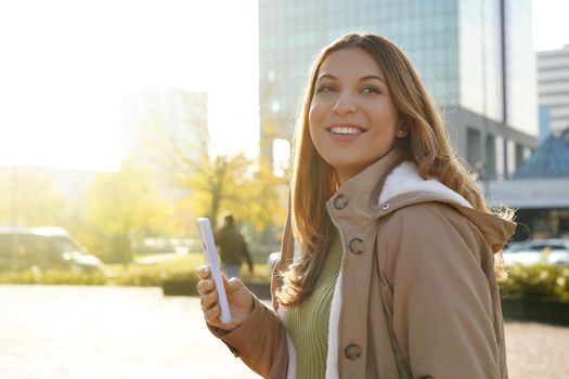 Smiling beautiful girl holding smartphone outside on sunset