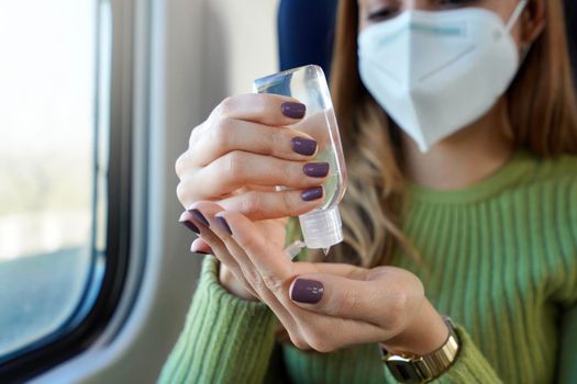 Business woman with medical face mask using alcohol gel sanitizing hands on public transport. Antiseptic, hygiene and health care concept. Focus on hand.
