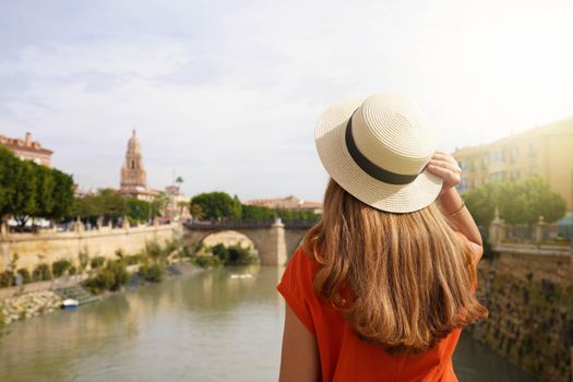 Visiting Murcia, Spain. Back view of tourist girl enjoying Murcia cityscape with Puente Viejo bridge and Cathedral bell tower, Spain.