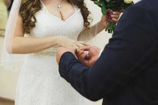 Newlyweds exchange rings, groom puts the ring on the bride's hand in marriage registry office.