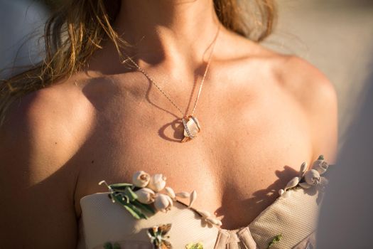 a medallion on a girl's neck during sunset.
