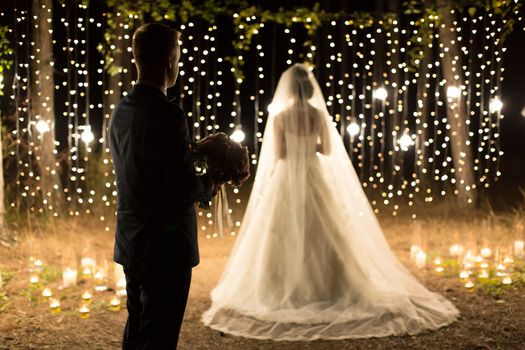 Wedding ceremony night. Meeting of the newlyweds, the bride and groom in the coniferous pine forest of candles and light bulbs