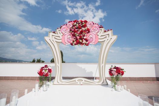 Arch with fresh red flowers on a background of sea and blue sky.