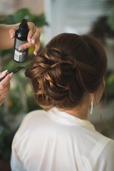 Master stylist makes the bride wedding hairstyle using spray lacquer fixing.