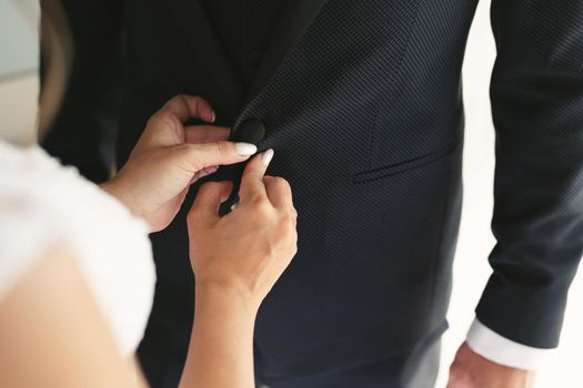 Bride helps the groom to button his jacket.