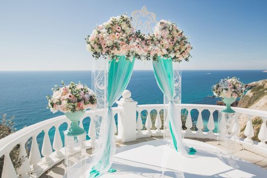 Elegant wedding arch with fresh flowers, vases on the background of the ocean and blue sky