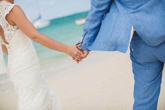 Beautiful gorgeous bride and stylish groom holding hands, on the background of a sea.