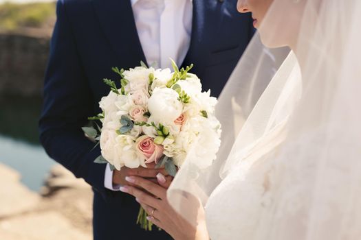 Delicate wedding bouquet of white, pink and powdery flowers in the hands of the bride