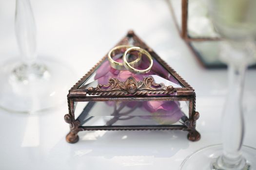 Wedding rings in a glass box with lilac rose petals.