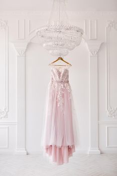 Rich pink wedding dress hangs on a chandelier in a white room.