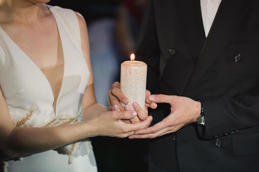 bride and groom hold a candle in their hands.