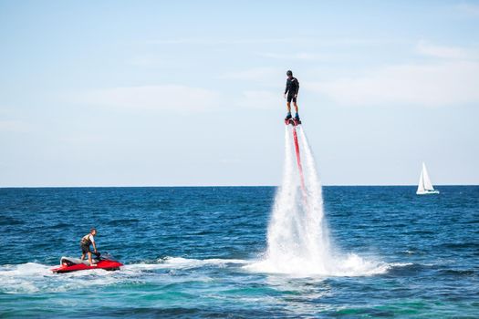 A rider on a flyboard in the ocean does difficult stunts.