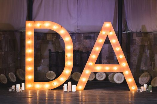 Wooden initials of the bride and groom with bright lights at the wedding