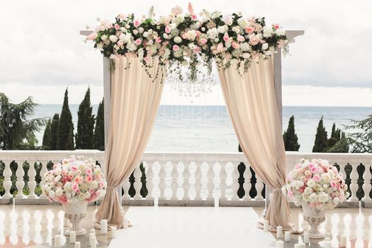 The wedding arch decorated with flowers stands in the luxurious area of the wedding ceremony
