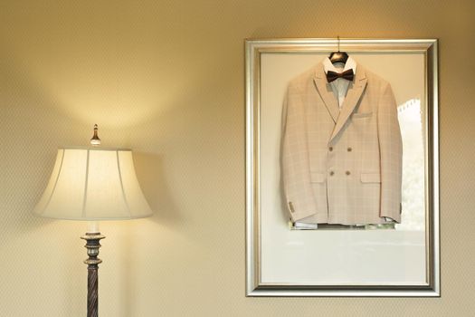 A light festive wedding jacket hangs on a wall lamp in a room with a table lamp