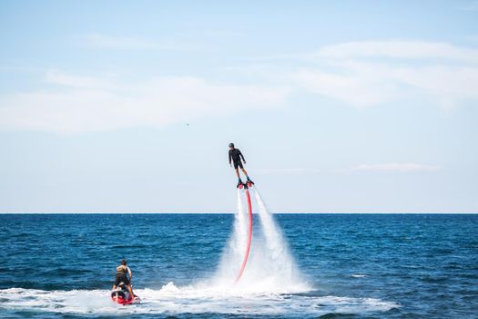 A rider on a flyboard in the ocean does difficult stunts.