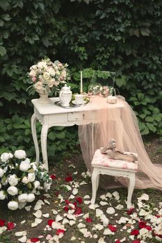 Romantic photo zone for the bride's wedding day gatherings. Table, flowers and rose petals in the forest