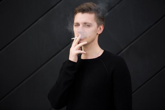 Young handsome guy Smoking a cigarette on black background.