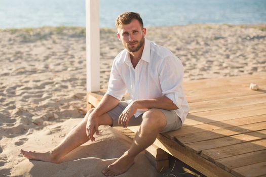 The man in the white shirt and shorts sitting on the beach