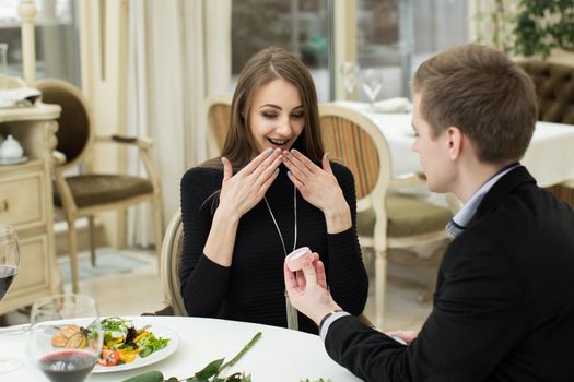 Marriage proposal at a restaurant. A man puts a ring on a woman's finger.