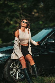 Young woman outdoors standing by her black car