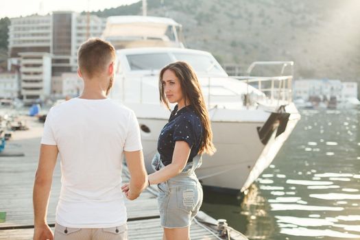 Lovers walk on the pier against the backdrop of yachts and boats