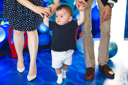 Little boy holds the hand of his mother and father and tries to take the first steps
