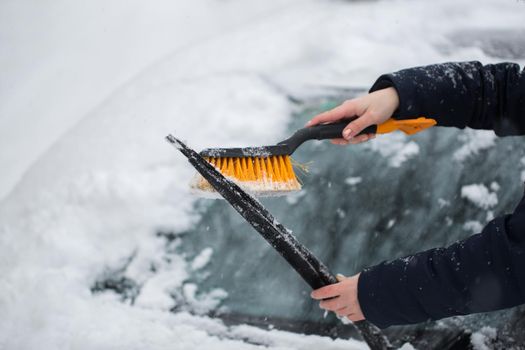 Woman cleaning snow from the car in the winter.