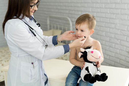 Pediatrician examining thyroid gland of little boy in clinic.