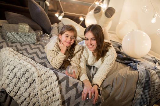 Beautiful mother and daughter lying on the bed on Christmas eve in the cozy interior of the house. New year.