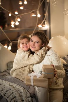 Beautiful mother and daughter opening a magical Christmas gift in the cozy interior of the house. New year.