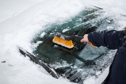 A woman removes snow from the windshield of a car.