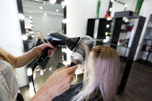 Drying long blonde hair with hair dryer and round brush.