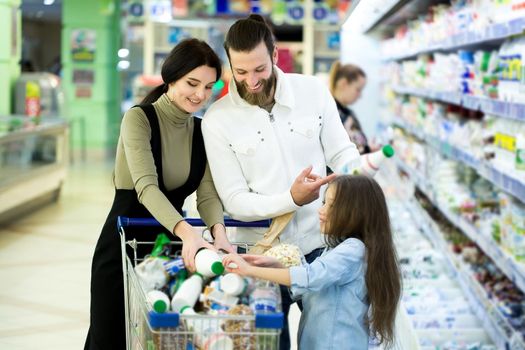 Young family with kid are choosing milk in supermarket