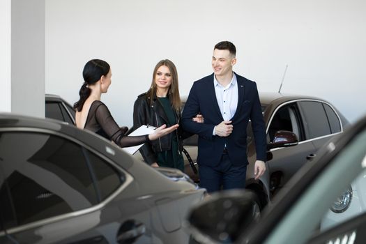 auto business, car sales - a happy couple with a car dealer in a car dealership or salon.
