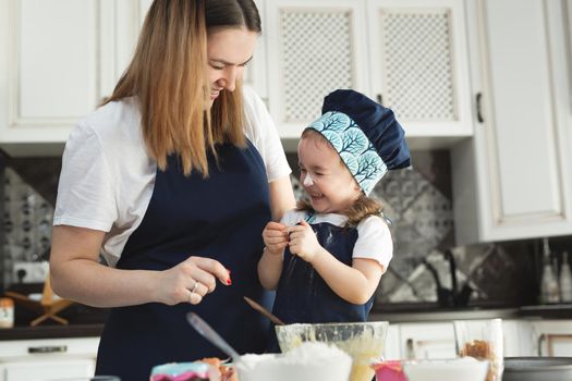 Cute little girl and her beautiful mom in matching aprons and caps play and laugh while kneading dough in the kitchen
