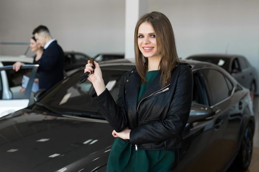 Beautiful woman or car salesman stand holding a new car remote key in a car showroom.
