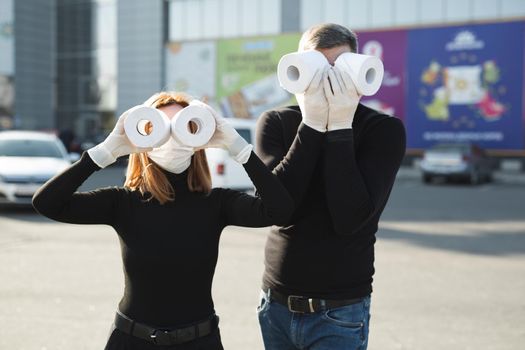 Woman and a man in a coronavirus face mask hold large rolls of toilet paper on a city street and indulge.
