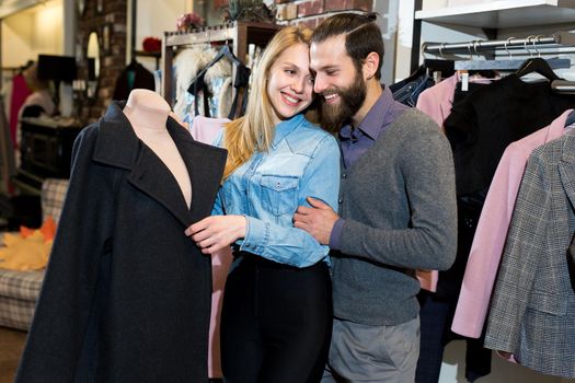 A young family, a man and a woman hug and choose a black coat in a clothing store