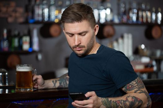 Young man sitting at bar counter with a pint of light beer.