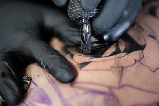 Close up image of the bearded tattoo male artist makes a tattoo on a female leg.
