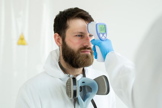 Doctor measures the temperature with an infrared thermometer to his colleague of infectious diseases. Portrait of a man doctor scientist in a lab coat. Concept of coronavirus
